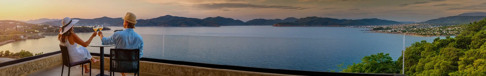 Pareja brindando con vino blanco en una terraza con vistas a una bahía al atardecer, en un momento de calma que forma parte de las experiencias GRAND.