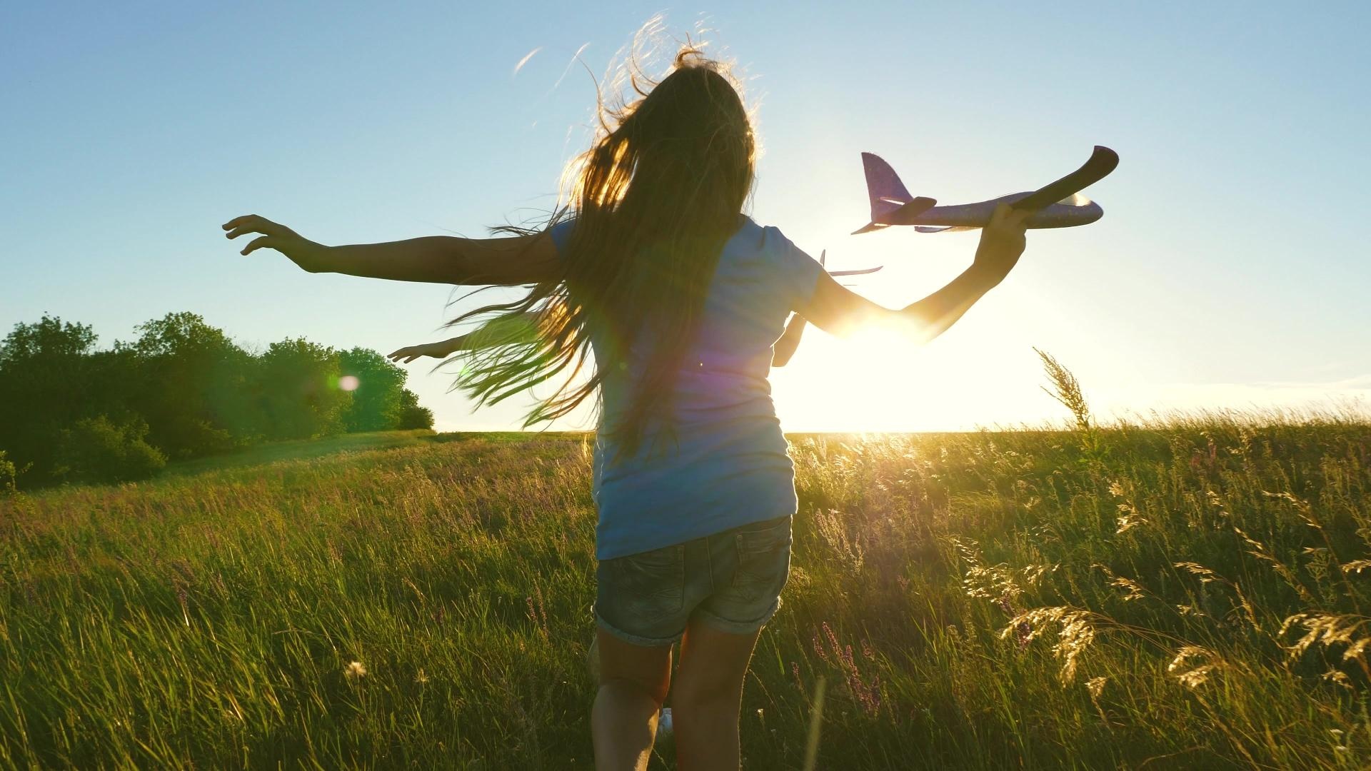 Niña con la maqueta de un avión en el campo al atardecer
