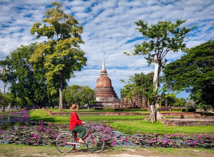 Tailandia, mujer con camiseta roja en bicicleta mirando templo budista