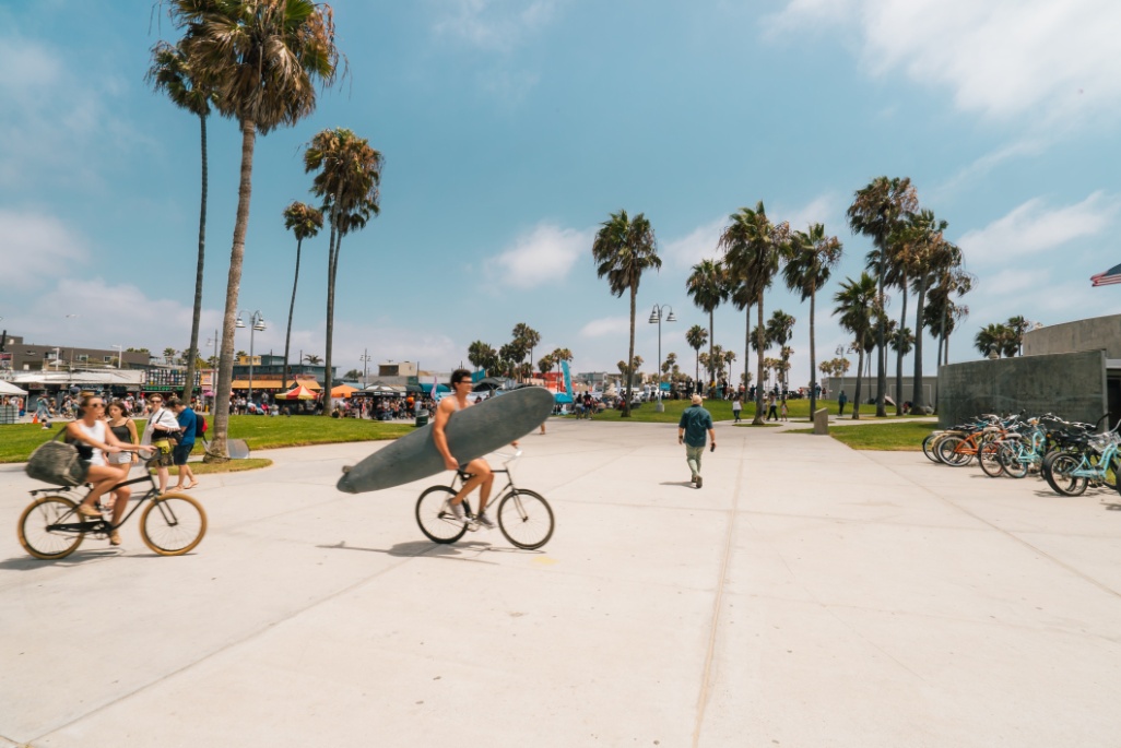 hombre en bicicleta con tabla de surf playa venice beach los angeles