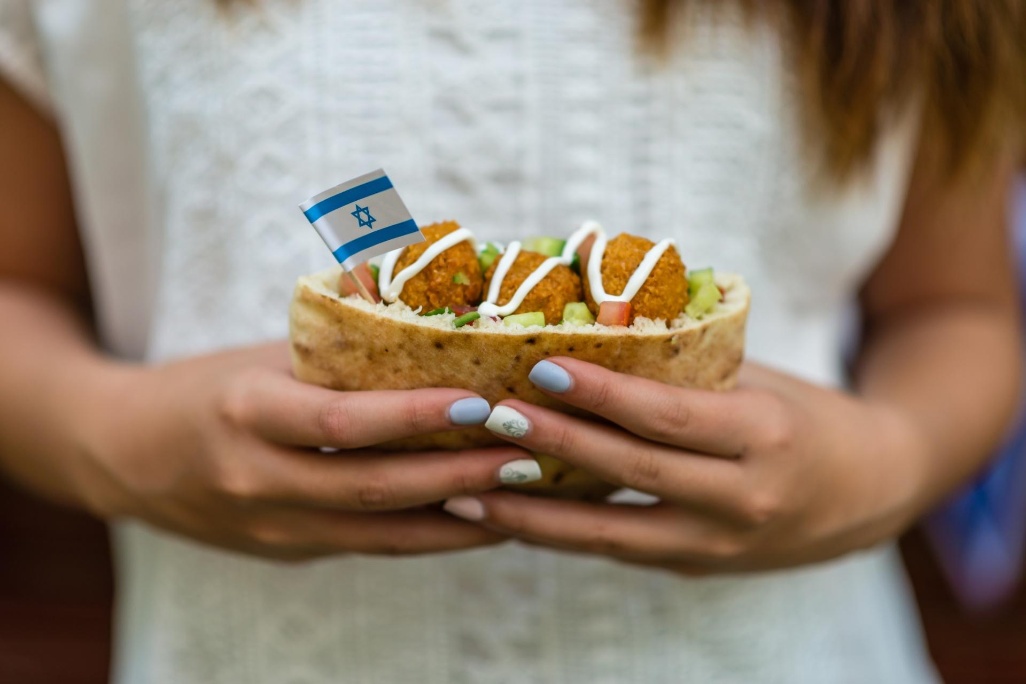mujer sosteniendo pan de pita con falafel y bandera de israel