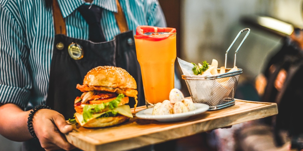 camarero sirviendo una hamburguesa guarnición y bebida en un restaurante