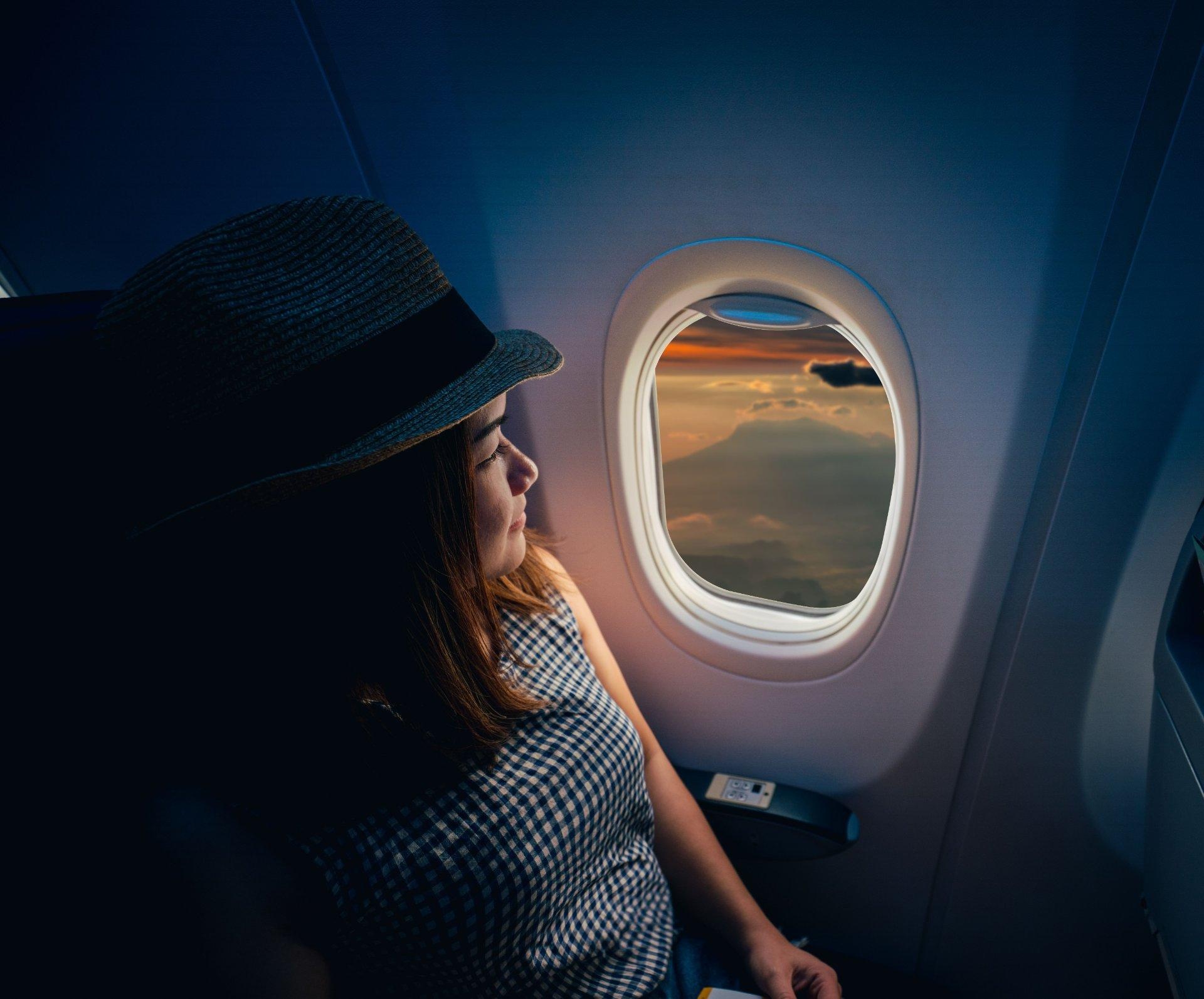 mujer con sombrero sentada en avión junto a ventanilla en vuelo de regreso
