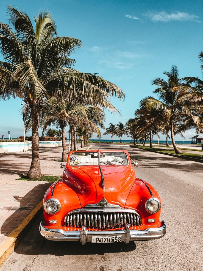 coche de época rojo en calle con palmeras en la habana cuba