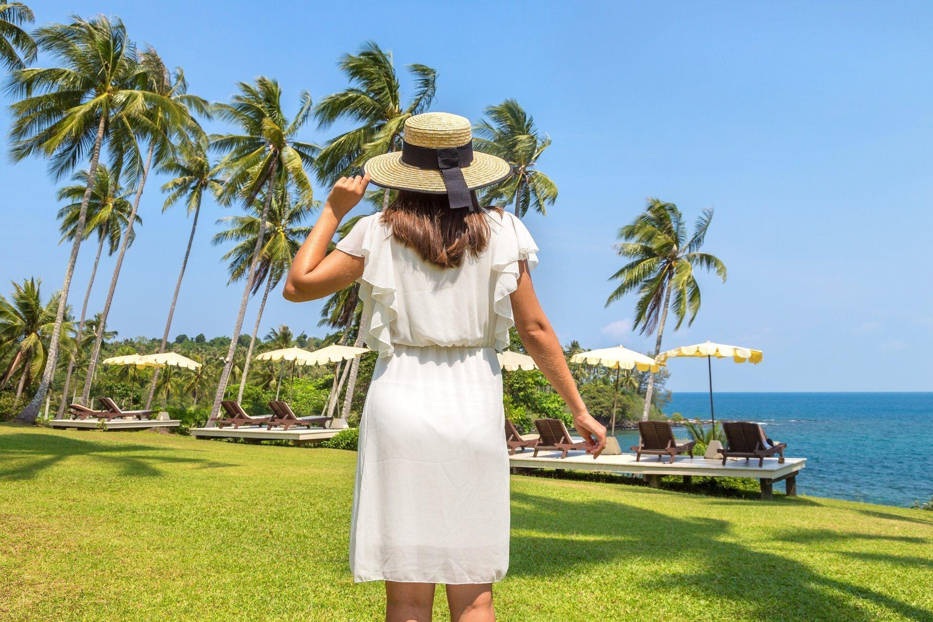 mujer con vestido blanco y sombrero frente al mar