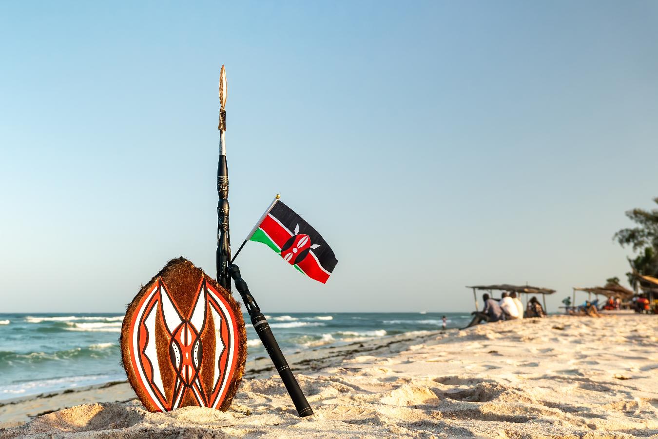 La lanza de Masai y la bandera nacional de Kenia en el fondo de un hermoso paisaje de playa