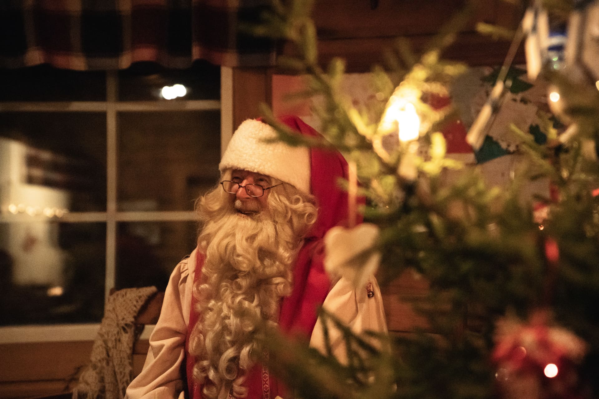 Papa Noel sonriendo detrás del árbol de navidad